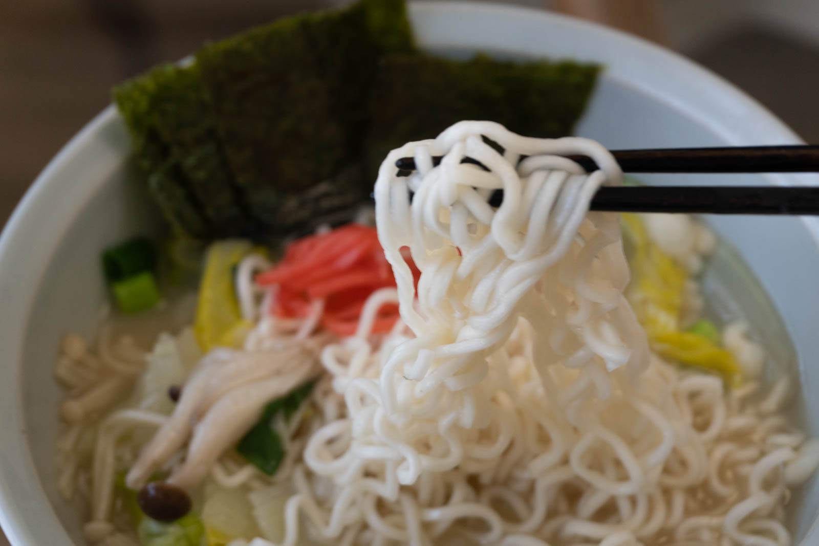 調理して器に盛ったラーメン。箸で麺を持ち上げているところ。野菜ときのこも入っていて、海苔や紅生姜がトッピングされている。