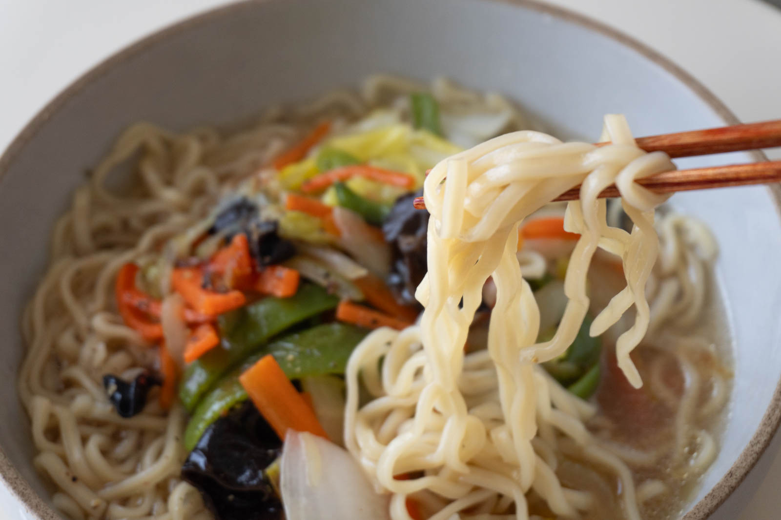 調理して器に盛ったラーメン。箸で麺を持ち上げているところ。炒めたピーマン、人参、キクラゲ、白菜、玉ねぎや黒胡椒をトッピング。