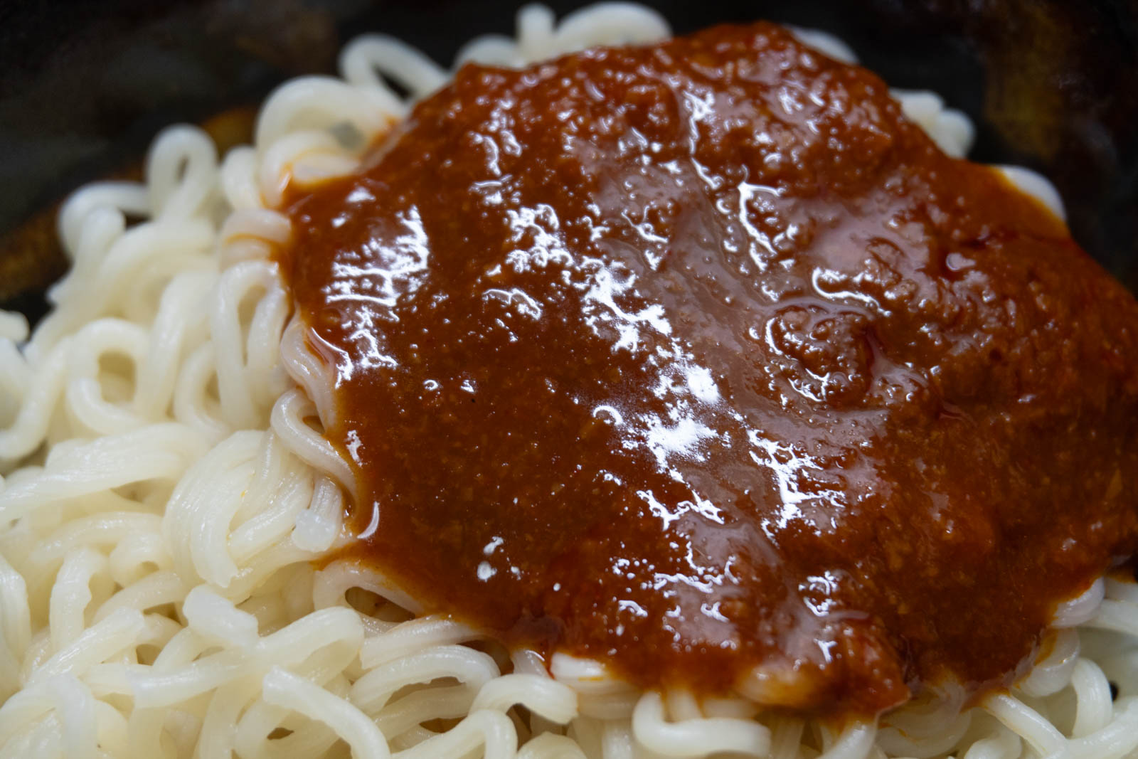 茹でた麺に付属のソースをかけたところ。赤茶色の濃いソースで細かい大豆そぼろが混ざっている。