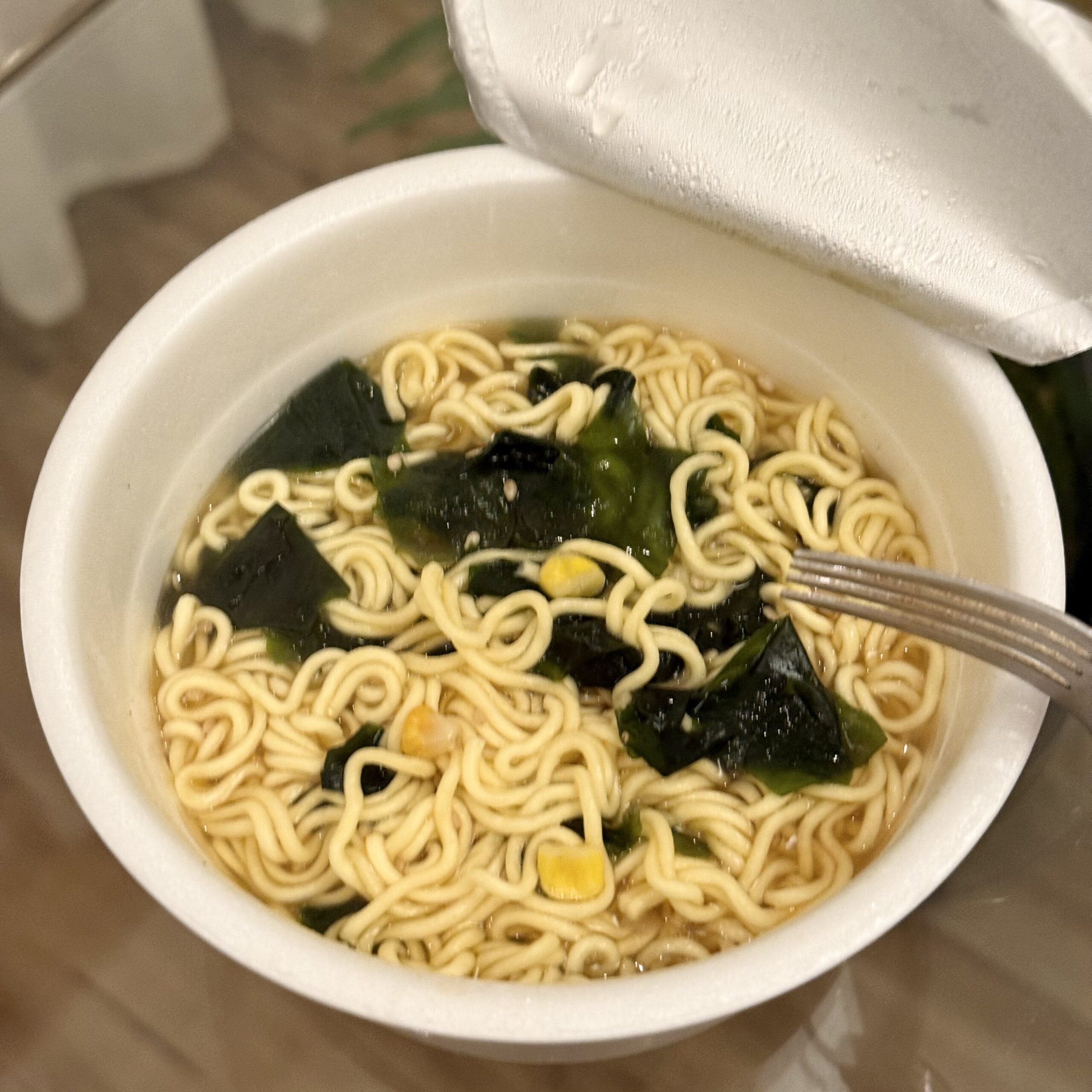 お湯を注いだカップ麺。麺とわかめ、コーンが浮いている。